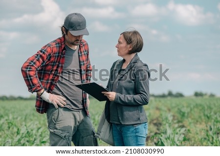 Mortgage loan officer assisting farmer in financial allowance application process, banker and farm worker in corn maize crop field. Royalty-Free Stock Photo #2108030990