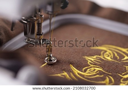 making of luxurious tiger head embroidery with golden yarn on brown merino wool fabric. close up view on working area of embroidery machine. fashion and chinese new year concept. selective focus