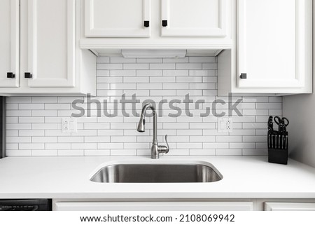 Kitchen sink detail shot with a subway tile backsplash, granite countertop, white cabinets, and a chrome faucet. Royalty-Free Stock Photo #2108069942