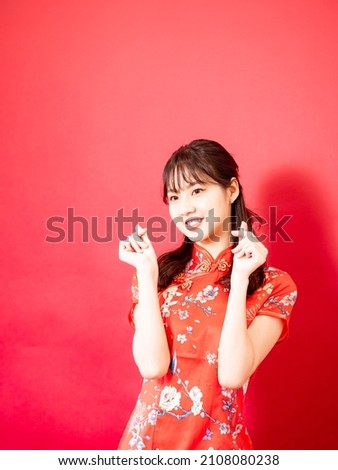 Young asian woman wear cheongsam showing mini heart sign isolated on red background.