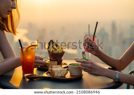 Young Asian woman friends celebrating dinner party meeting at skyscraper rooftop restaurant bar in metropolis at summer sunset. Beautiful girl enjoy outdoor lifestyle together on holiday vacation. Royalty-Free Stock Photo #2108086946