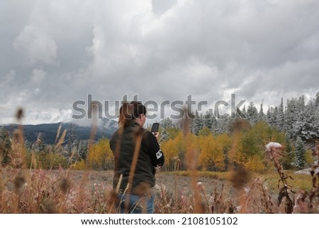 A female standing in a sagebrush patch viewing the colorful aspen trees looking away from the camera taking a picture in late fall near Jackson, Wyoming