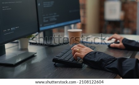 Closeup of developer hands typing code on keyboard while looking at computer screens with programming interface. Software programmer sitting at desk with clipboard writing algorithm. Royalty-Free Stock Photo #2108122604