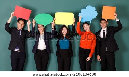 Portrait studio shot group of Asian professional male female teacher or college students in formal suit outfit standing smiling look at camera holding conversation sign on green chalkboard background.