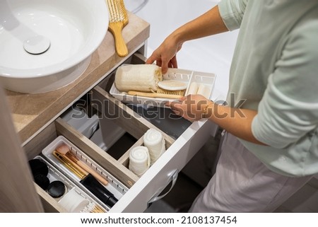 Top view of woman hands neatly organizing bathroom amenities and toiletries in drawer or cupboard in bathroom. Concept of tidying up a bathroom storage by using Marie Kondo's method. Royalty-Free Stock Photo #2108137454