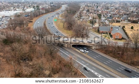 An aerial view over a parkway in a suburban neighborhood on Long Island, NY on a cloudy Sunday with some traffic. It is winter and the trees and landscape is brown and dry.