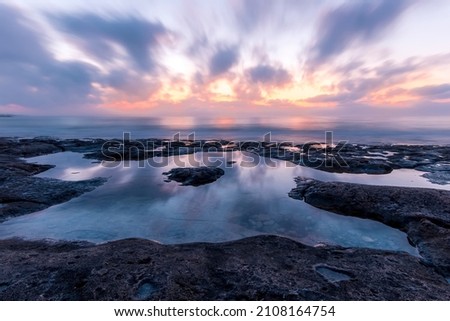 Twilight scenic sea landscape with beautiful shore, blurred flying dramatic blue clouds, amazing shoreline and sunset on horizon