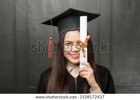 Portrait of young woman in graduation gown smiling and cheering on black background 
