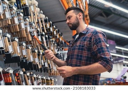 male builder in a hardware store chooses a hammer Royalty-Free Stock Photo #2108183033