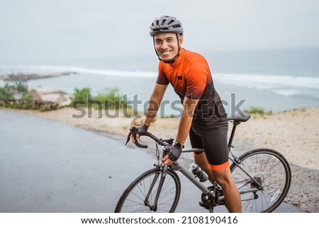 male asian cyclist with red and black jersey standing on his bike Royalty-Free Stock Photo #2108190416