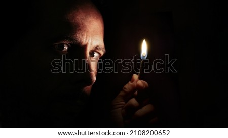 Worried man looking at the camera with a match in the dark. Blackout concept. Royalty-Free Stock Photo #2108200652
