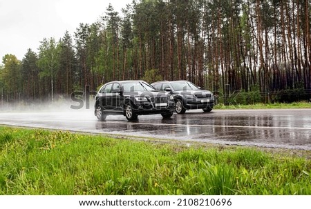 Two modern crossover cars drive on a wet country road in rainy weather against the backdrop of a forest. Royalty-Free Stock Photo #2108210696