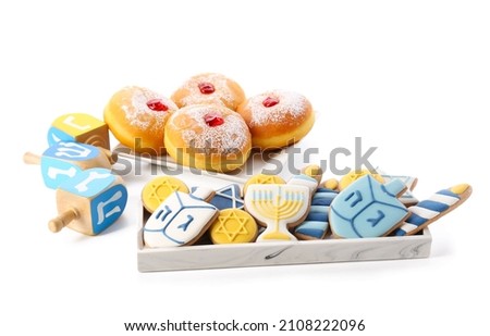 Tasty cookies and donuts for Hanukkah celebration with dreidels on white background