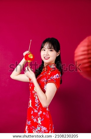 Beautiful Asian girl in traditional cheongsam on red background holding a lantern. The Chinese characters translated as:blessing.