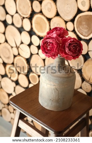 Vase with beautiful flowers on stool near wooden wall