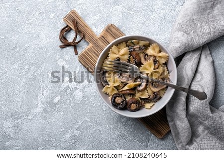Top view of tasty italian farfalle pasta and champignon mushrooms with cream sauce in bowl on grey concrete background Royalty-Free Stock Photo #2108240645
