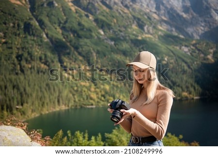 Photographer tourist traveler standing on green top on mountain holding in hands digital photo camera. Hiker taking  photography, girl enjoy nature panoramic landscape in trip