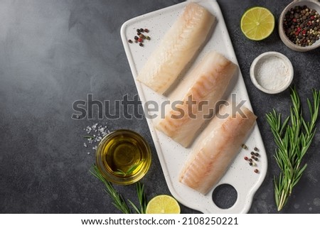 Fillet of white cod fish with lime, rosemary, spices on a cutting board. Healthy seafood. dark background with ingredients for cooking