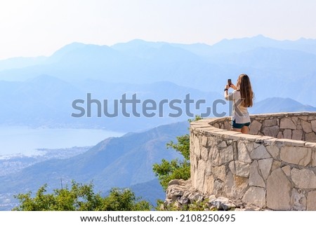 Young woman taking photo of Kotor bay from the viewpoint in mountains on sunny clear day.