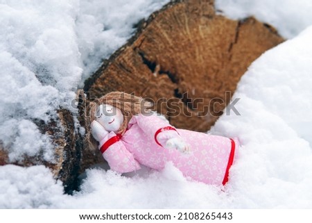 A sleeping toy girl in pink dress the forest. A toy in the snow.