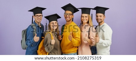 Education and success: Happy confident multiracial male and female university students, classmates and best friends in graduate hats give thumbs up standing together on purple color studio background