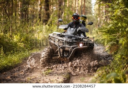 a quad moving trough the mud with two riders on it Royalty-Free Stock Photo #2108284457