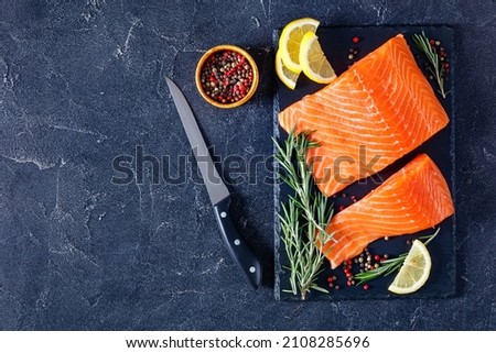 salmon fillet pieces with peppercorn, rosemary and lemon on black slate board on a grey concrete table, horizontal view from above, flat lay, free space