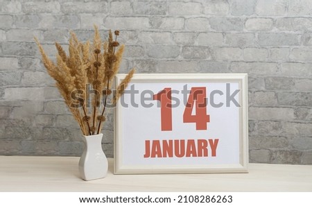 january 14. 14th day of month, calendar date.  White vase with ikebana and photo frame with numbers on desktop, opposite brick wall. Concept of day of year, time planner, winter month.