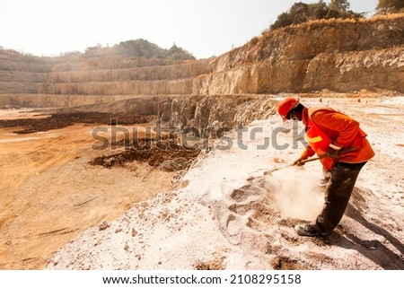 An identified miner wearing a face mask, helmet, and protective equipment working with a mining tool in dusty and baking hot at a mining quarry. Work, industry concepts.