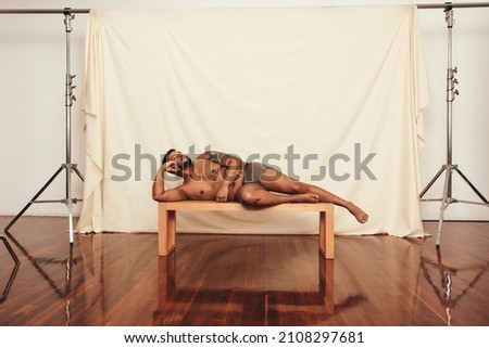 Comfortable in underwear. Body positive young man looking relaxed while lying shirtless on a bench in a modern studio. Self-confident young man embracing his natural body. Royalty-Free Stock Photo #2108297681