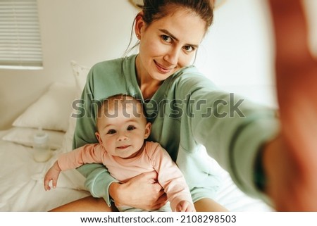 Blogger mom taking a selfie with her baby at home. Millennial mom taking a picture while sitting on the bed with her baby. Influencer mom creating content for her motherhood blog.
