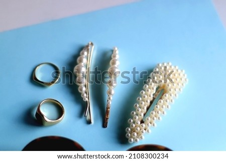 Round sunglasses, pearl hair clips and gold rings on bright blue background. Selective focus.