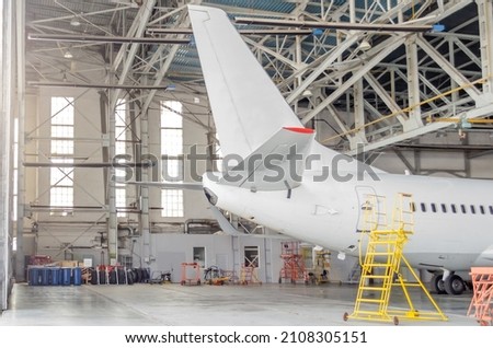 Passenger aircraft on maintenance of engine and fuselage repair in airport hangar, tail view Royalty-Free Stock Photo #2108305151