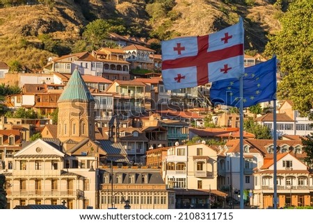 Georgian and European Union waving flags in Georgian capital city with Tbilisi old town at background. Georgian politics and international affairs concept