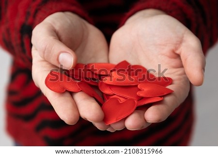 Closeup of woman who wearing red sweater and holding heap of little decor hearts
