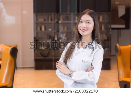 Asian woman doctor Standing smile in a good mood with arms crossed in the office room in the hospital. Wearing a white robe and stethoscope. Royalty-Free Stock Photo #2108322170