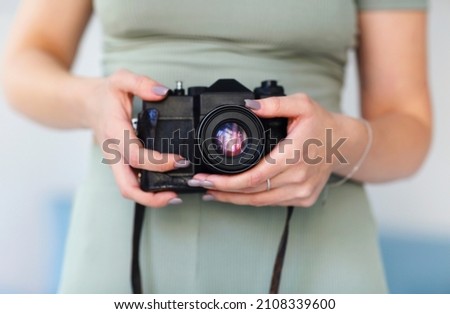 Young woman photographer taking photo picture with camera indoors, female photographing during professional photoshoot in studio, looking into lens, standing against gray wall. Hobby concept