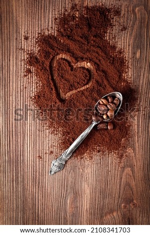 Coffee beans in metal spoon and coffee powder with heart shape on wooden background