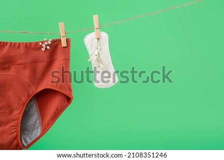Period panties, pad and gypsophila flowers hanging on rope against green background, closeup