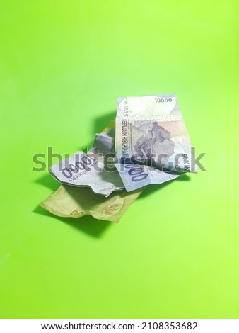 several pieces of Indonesian state banknotes in rupiah currency, in untidy condition, photographed on isolated green background