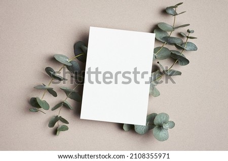 Invitation or greeting card mockup with natural eucalyptus twigs on paper background.