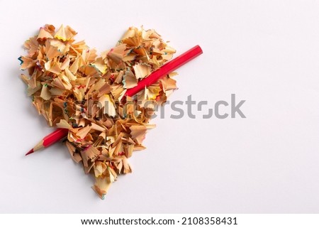 The heart of pencil shavings is pierced with a red pencil like an arrow. Valentine's Day. Royalty-Free Stock Photo #2108358431