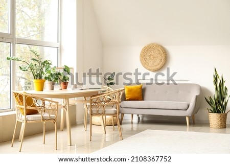 Interior of light living room with wooden table, grey sofa and houseplants