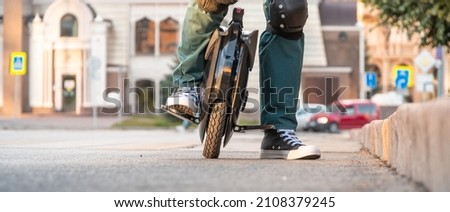 Rider's legs in protective gear on an electric unicycle (EUC). Driving around the city on an electric monowheel. Royalty-Free Stock Photo #2108379245