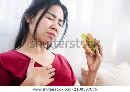 Asian woman having heartburn, acid reflux after eating burger, eating junk food concept  Royalty-Free Stock Photo #2108387096