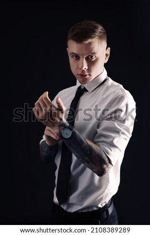 Young man with tattoos and wristwatch on black background
