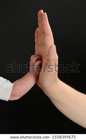 Baby and adult hands clashing. Body parts isolated on black background.