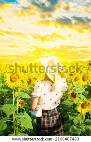 A young Asian female tourist takes a picture with a field of yellow sunflowers at sunset.