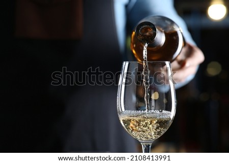 Bartender pouring white wine from bottle into glass indoors, closeup. Space for text