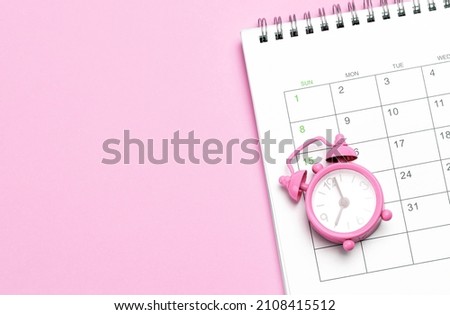 Pink alarm clock and calendar on a pink background. Concept days of menstruation or menopause. Template Copy space for text. mock-up. Royalty-Free Stock Photo #2108415512